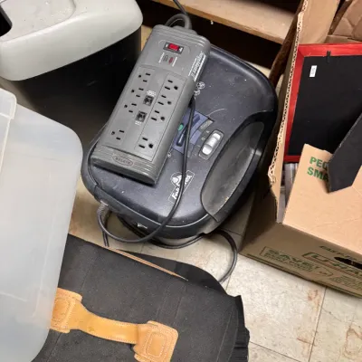 Sale Photo Thumbnail #98: Belkin SurgeMaster II power strip resting on a Fellowes paper shredder, shown alongside a black carrying bag and other office supplies.