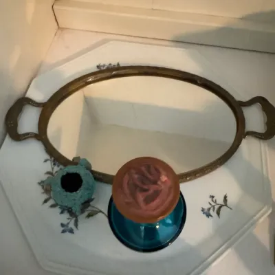 Sale Photo Thumbnail #184: Vintage brass-framed vanity mirror tray with handles, displayed alongside a small blue ceramic vessel and a decorative glass piece on a floral ceramic platter.