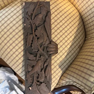 Sale Photo Thumbnail #277: Antique hand-carved dark wood architectural fragment or panel, featuring intricate leaf and vine motifs, resting on a plaid armchair.