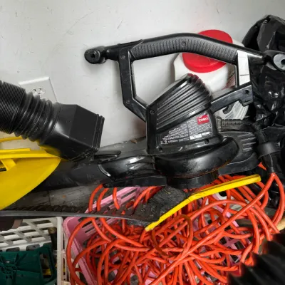 Sale Photo Thumbnail #87: Toro electric leaf blower and vacuum, showing signs of use, pictured with a coiled orange extension cord and other garage items.