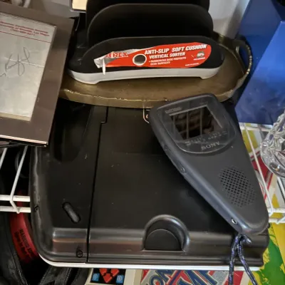 Sale Photo Thumbnail #161: Vintage Sony Watchman portable television resting on a black electronic device, alongside an office desk organizer and other miscellaneous items.