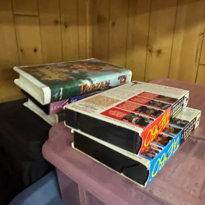 Sale Photo Thumbnail #135: A small collection of VHS tapes, including Disney's Tarzan and Tae Bo workout videos, resting on plastic storage bins.