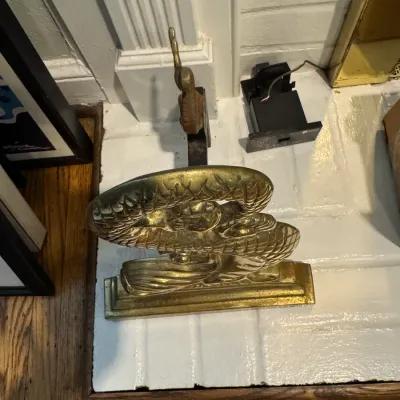 Sale Photo Thumbnail #56: Vintage brass fireplace andiron featuring a stylized dragon or serpent design, resting on a painted brick hearth.