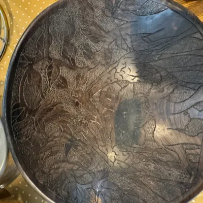 Sale Photo Thumbnail #305: Hand-carved dark wood bowl featuring detailed wildlife and foliage motifs, showing some surface wear.