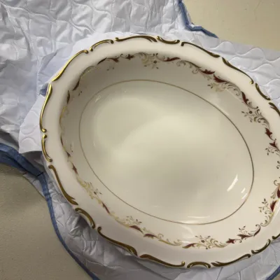 Sale Photo Thumbnail #136: Vintage porcelain oval serving bowl featuring a scalloped rim with gold trim and delicate floral scrollwork in burgundy and gold.