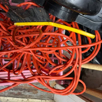 Sale Photo Thumbnail #88: Tangled orange heavy-duty extension cord resting in a pink plastic crate alongside a yellow-handled wire brush and other workshop tools.