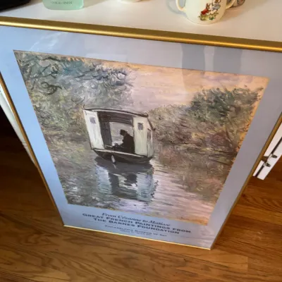 Sale Photo Thumbnail #231: Framed exhibition poster for "Great French Paintings from the Barnes Foundation" at the Philadelphia Museum of Art, featuring Claude Monet's "The Studio Boat," displayed alongside various ceramic tableware items.