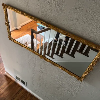 Sale Photo Thumbnail #210: Vintage rectangular wall mirror featuring an ornate, gilded frame with scrollwork details, mounted horizontally on a textured wall.