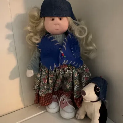Sale Photo Thumbnail #192: Vintage soft-sculpture doll with blonde curls, wearing a denim cap, blue vest, and floral skirt, accompanied by a matching plush dog.