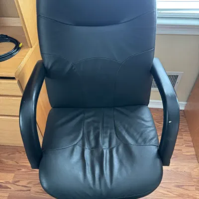 Sale Photo Thumbnail #41: Black faux leather high-back office chair with padded armrests and a wheeled base, showing some wear on the seat.