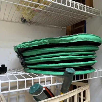 Sale Photo Thumbnail #71: Collapsible green fabric garden waste bin, shown folded flat on a white wire shelf.