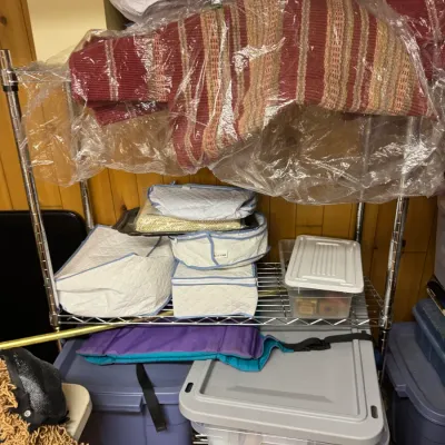 Sale Photo Thumbnail #131: Chrome wire shelving unit holding various household items, including plastic storage bins, quilted storage bags, and a striped textile wrapped in plastic.