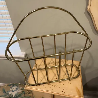 Sale Photo Thumbnail #144: Vintage mid-century modern brass wire magazine rack with a curved carrying handle, resting on a small wooden chest.