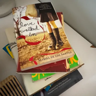 Sale Photo Thumbnail #218: Stack of assorted paperback and hardcover books, featuring "Love Walked In" by Marisa de los Santos on top.