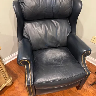 Sale Photo Thumbnail #21: Traditional navy blue leather wingback recliner featuring brass nailhead trim, showing significant wear and fading on the seat cushion.