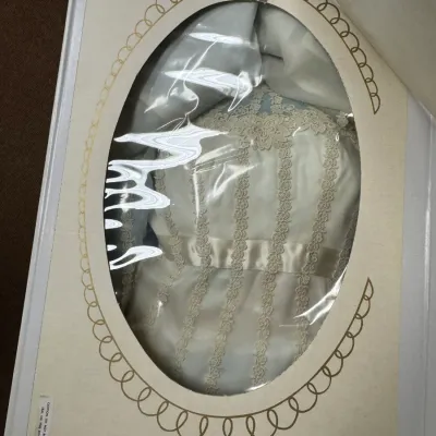 Sale Photo Thumbnail #153: Vintage wedding dress with lace detailing and a satin sash, preserved in a cardboard display box with an oval viewing window.