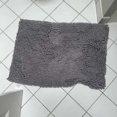 Sale Photo Thumbnail #208: Grey chenille microfiber bath mat with a textured, shaggy pile, shown on a white tiled floor.