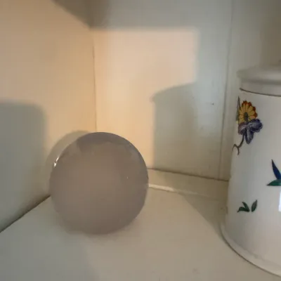 Sale Photo Thumbnail #188: Translucent frosted glass sphere decorative object, displayed on a white shelf next to a floral ceramic canister.