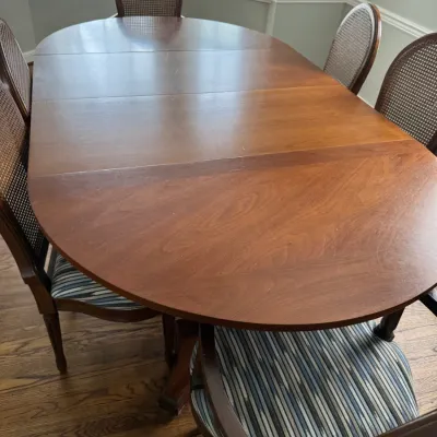 Sale Photo Thumbnail #329: Mid-century modern style oval wooden dining table with extension leaves, paired with cane-back chairs featuring striped upholstered seats.