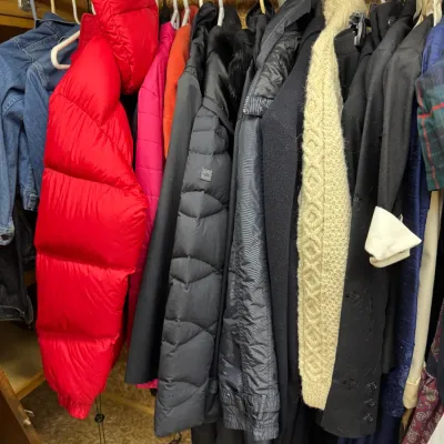 Sale Photo Thumbnail #91: Assorted outerwear hanging in a closet, featuring a bright red puffer jacket, a black The North Face quilted coat, a cream cable-knit sweater, and various other jackets.