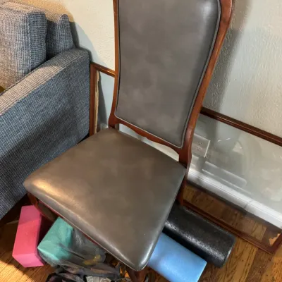 Sale Photo Thumbnail #294: Vintage high-back dining chair featuring a carved wooden frame with a scalloped top rail and grey faux leather upholstery on the seat and backrest.