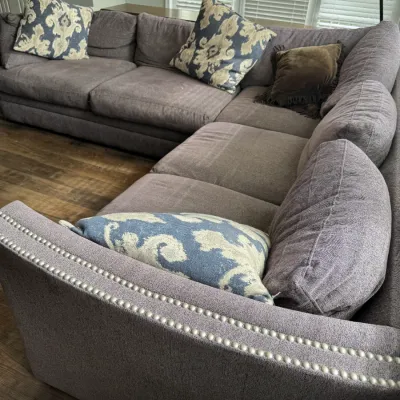Sale Photo Thumbnail #318: Large L-shaped sectional sofa in a textured gray fabric, featuring double rows of silver nailhead trim along the armrests and styled with patterned blue and cream throw pillows.