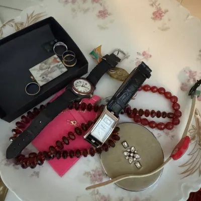 Sale Photo Thumbnail #50: Assorted vintage jewelry and watches, including a red beaded necklace, a rectangular silver-tone watch with a black leather strap, and a round Wenger watch, displayed on a floral porcelain plate.