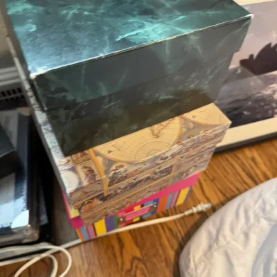 Sale Photo Thumbnail #246: Stack of decorative storage boxes, including a green marble-patterned box, a vintage map-themed box, and a colorful striped box.