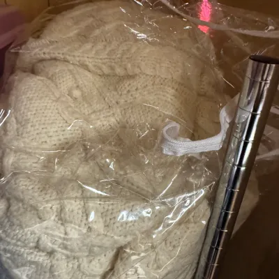 Sale Photo Thumbnail #134: Cream-colored cable-knit blanket or throw stored inside a zippered clear plastic bag.