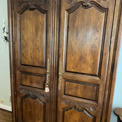 Sale Photo Thumbnail #297: Large French Provincial style oak armoire featuring ornate floral carvings, arched door panels, and decorative brass hardware.