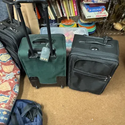Sale Photo Thumbnail #115: Three pieces of rolling luggage, including a green Tumi suitcase with a telescoping handle and two black suitcases, showing some wear from use.