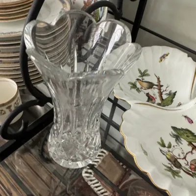 Sale Photo Thumbnail #342: Vintage cut crystal vase with a scalloped rim, displayed alongside bird-themed porcelain plates on a black metal baker's rack.