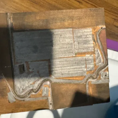 Sale Photo Thumbnail #278: Vintage woodblock printing plate featuring a metal-faced design mounted on a thick wooden block, showing signs of age and use.