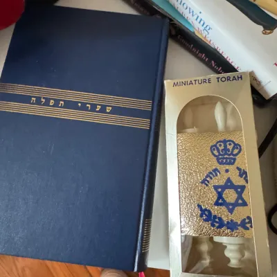 Sale Photo Thumbnail #220: Blue hardcover Jewish prayer book with gold lettering alongside a boxed miniature Torah scroll souvenir.