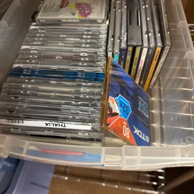 Sale Photo Thumbnail #133: Collection of assorted music CDs in jewel cases, including a TDK CD-R, stored in a clear plastic bin.