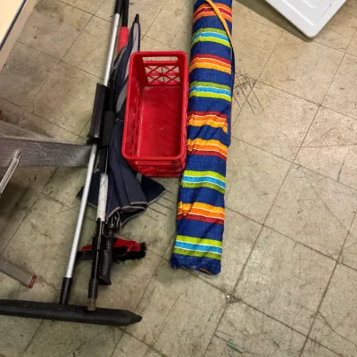 Sale Photo Thumbnail #97: Assorted household and outdoor items, including a red plastic crate, a striped beach umbrella in its carrying bag, and various long-handled cleaning tools.