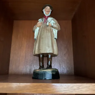 Sale Photo Thumbnail #289: Vintage hand-painted ceramic figurine of a shepherd holding two lambs, displayed on a wooden shelf.