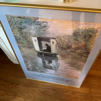 Sale Photo Thumbnail #216: Framed exhibition poster for "Great French Paintings from the Barnes Foundation" at the Philadelphia Museum of Art, featuring Claude Monet's "The Studio Boat," presented in a gold-toned metal frame.