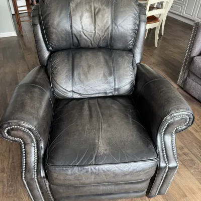 Sale Photo Thumbnail #319: Distressed dark grey leather recliner featuring rolled arms with silver nailhead trim and a plush, segmented backrest.