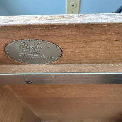 Sale Photo Thumbnail #334: Baker Furniture oval metal maker's mark embedded in the wooden drawer side of a vintage furniture piece.