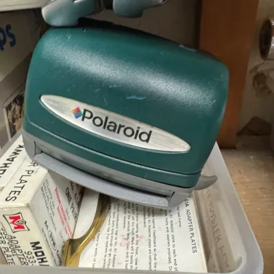 Sale Photo Thumbnail #4: Vintage Polaroid JoyCam instant camera in teal, sitting on a plastic bin of vintage adapter plates.