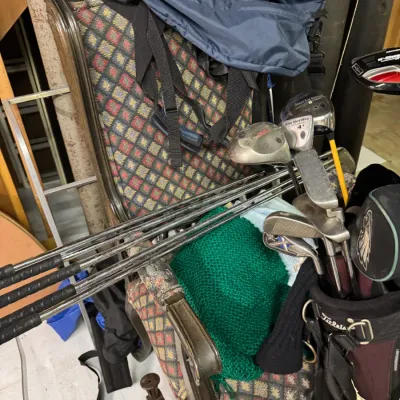Sale Photo Thumbnail #109: Assorted golf clubs in a Titleist bag, including a Callaway Great Big Bertha driver, shown alongside a patterned armchair and a blue duffel bag.