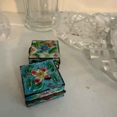 Sale Photo Thumbnail #191: Pair of vintage miniature cloisonné enamel pill boxes featuring colorful floral designs, displayed alongside cut glass tableware.