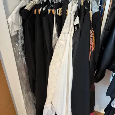 Sale Photo Thumbnail #159: Assorted men's and women's apparel, including blazers, dress shirts, and outerwear, hanging on a closet rod.