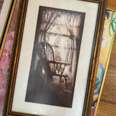 Sale Photo Thumbnail #233: Framed pastel or charcoal drawing depicting a rocking chair by a window, signed by R. Baron, housed in a gilded wood frame.