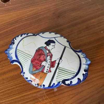 Sale Photo Thumbnail #288: Vintage French Quimper style hand-painted ceramic dish, featuring a traditional Breton figure with a walking stick and a blue scalloped border.
