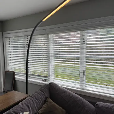 Sale Photo Thumbnail #68: Modern black LED arc floor lamp with a slim, curved profile, shown illuminated over a living room sofa.