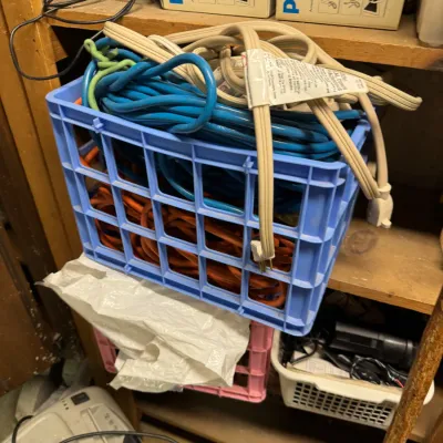 Sale Photo Thumbnail #99: Assorted extension cords in blue, orange, and beige, organized inside a light blue plastic milk crate.