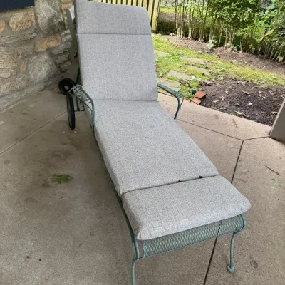 Sale Photo Thumbnail #310: Vintage wrought iron chaise lounge with a green finish, rear wheels for mobility, and a modern grey outdoor cushion.