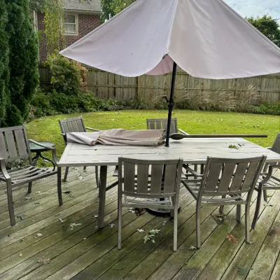 Sale Photo Thumbnail #337: Modern gray metal outdoor dining set featuring a rectangular slatted table, six matching armchairs, and a large light gray patio umbrella.